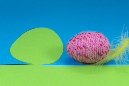 Easter egg and feather in close-up as a set of decoration on spring theme in Christianity, placed on green background with flower cutout of blue paperの写真素材