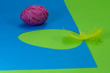 Easter egg and feather in close-up as a set of decoration on spring theme in Christianity, placed on green background with flower cutout of blue paperの写真素材