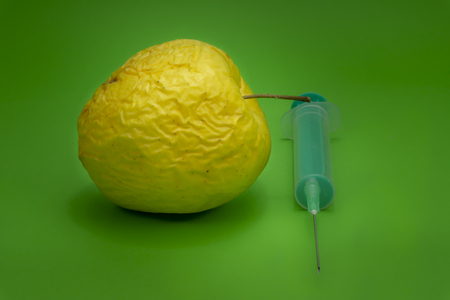 Old withered fresh apple with hypodermic needle, concept of healthcare, plastic surgery, treatment, research and medicine over a green backgroundの写真素材