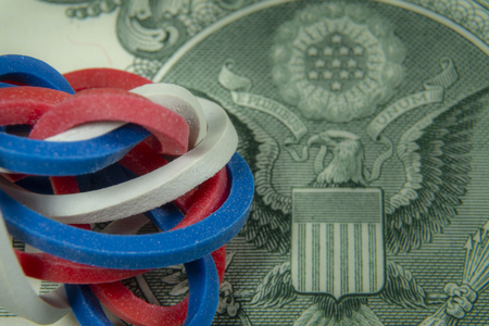 Twisted red, white and blue rubber bands on dollar banknote in a close up view, conceptual of trade, business, investment, savings, retirement, finance and moneyの写真素材