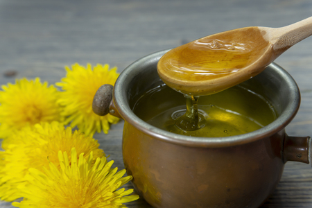 Pot of honey dripping off a spoon with colorful yellow spring dandelions alongside in a healthy diet conceptの写真素材