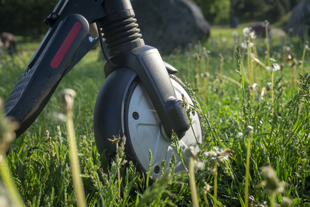 Front wheel of a scooter on meadow grass in a close up low angle view with withered wildflowersの写真素材