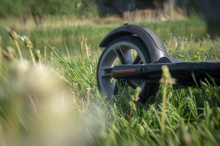 Rear wheel of a scooter on meadow grass in a close up low angle view with withered wildflowers