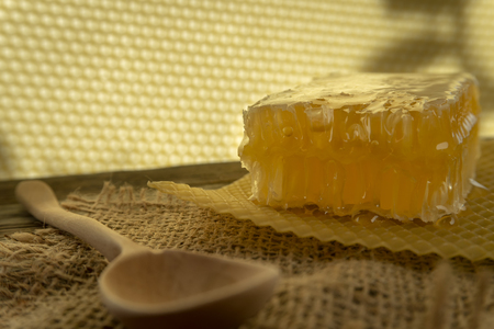 Block of natural honey comb with healthy fresh honey alongside a wooden spoon on a square of rustic hessian cloth with copy spaceの写真素材