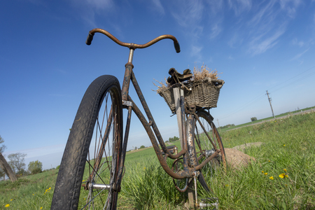Rusty old bicycle in a country meadow or farm field with lush green spring grass viewed low angle against a blue sunny skyの写真素材