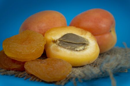 Dried apricots and fresh whole and sliced halved apricots on a square of rustic hessian cloth in a close up viewの写真素材