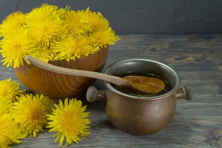 Pot of honey dripping off a spoon with colorful yellow spring dandelions alongside in a healthy diet conceptの写真素材