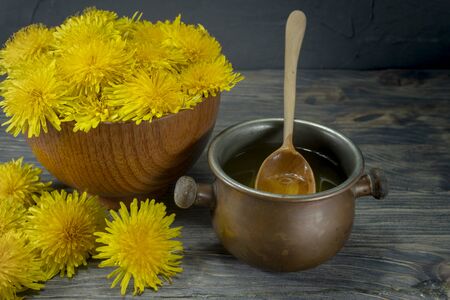 Pot of honey dripping off a spoon with colorful yellow spring dandelions alongside in a healthy diet conceptの写真素材