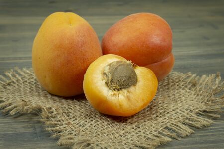 Fresh whole and sliced halved apricots on a square of rustic hessian cloth in a close up viewの写真素材