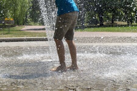 Barefoot person running through a fountain into the spray of water in a low angle view of their legsの写真素材
