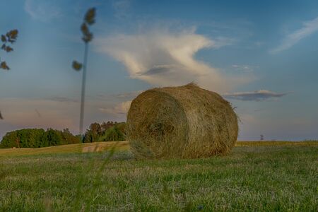 Large round hay bale on a farm field at sunset viewed low angle across the stubble against colorful pink clouds in a blue skyの写真素材