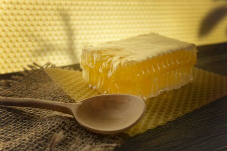 Block of natural honey comb with healthy fresh honey alongside a wooden spoon on a square of rustic hessian cloth with copy spaceの写真素材