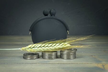 Single piece of wheat laying across stack of silver coins, small frame purse in background, grains prices conceptの写真素材