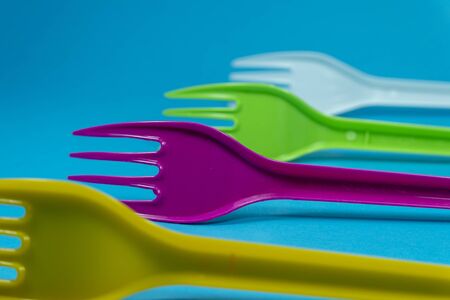 Yellow purple green and white cutlery plastic forks arranged on blue background. Color trends and recycling, plastic waste problem conceptsの写真素材
