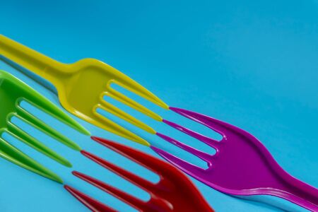 Yellow purple, red green and white cutlery plastic forks arranged on blue background. Color trends...