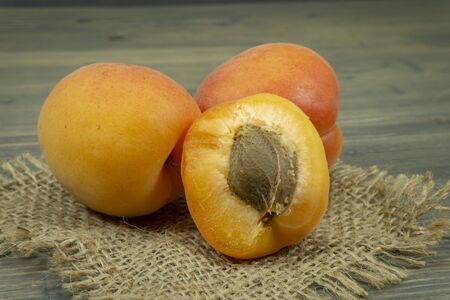 Fresh whole and sliced halved apricots on a square of rustic hessian cloth in a close up viewの写真素材