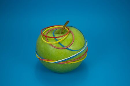 Green apple tied in colorful rubber bands over a blue background. Simplicity back to school or diet, aerobic concept with copy space for textの写真素材