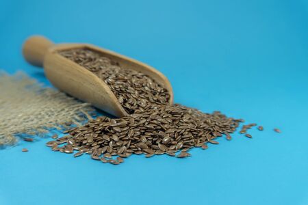 Flax seeds spilling from a wooden scoop, copy space on blue backgroundの写真素材