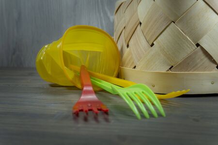 Colorful plastic forks and tipped wicker basket on rustic wooden background in close-up. Plastics recycling concept imageの写真素材