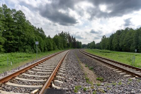 Curving railroad track through the forest against a blue sky and white clouds, low angle viewの写真素材