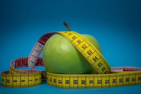 Weight loss and healthy diet concept with measuring tape and green apple on blue backgroundの写真素材