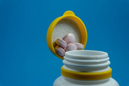 Medicine pills spilling out of a white bottle on a blue backgroundの写真素材