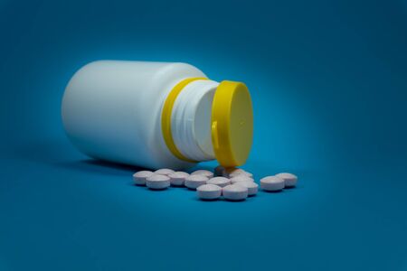 Medicine pills spilling out of a white bottle on a blue backgroundの写真素材