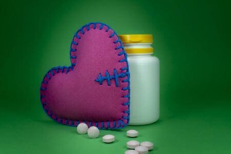 Medical pills and medical bottle near heart sing on a green background. Drug therapy and blood pressure conceptの写真素材