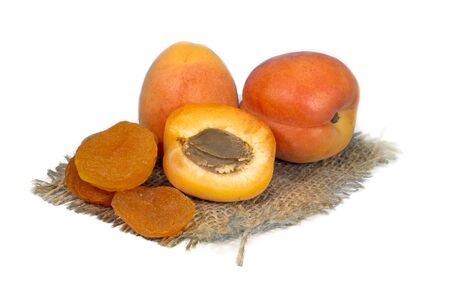Dried apricots and fresh whole and sliced halved apricots on a square of rustic hessian cloth in a close up view, isolated on whiteの写真素材