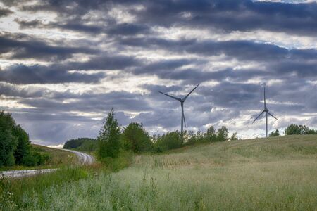 Road and wind power turbines for electric power generation over hills and gloomy rain clouds surroundingの写真素材