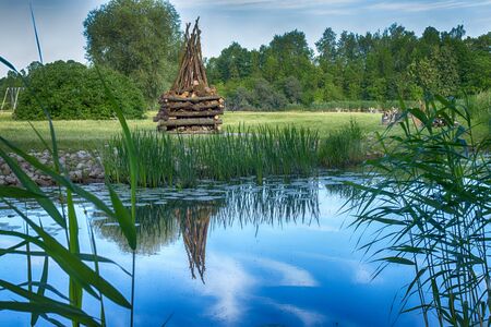 Tranquil lake with large ready built bonfire on the further shore waiting to be lit in the evening for a celebration or partyの写真素材