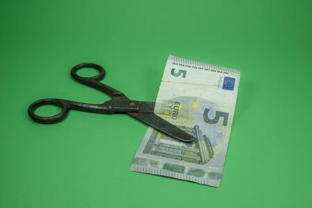 Old vintage scissors cut five EUR banknote over green background. European Central Bank interest rate cuts conceptの写真素材