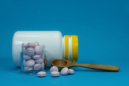 Medicine pills spilling out of a white bottle on a blue backgroundの写真素材