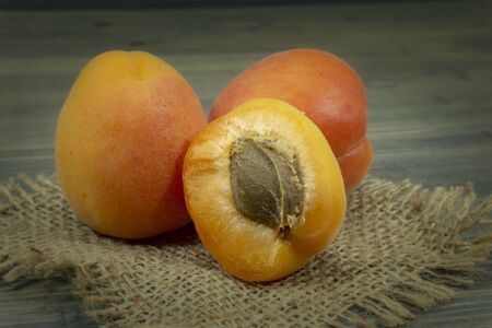 Fresh whole and sliced halved apricots on a square of rustic hessian cloth in a close up viewの写真素材