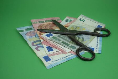 Old vintage scissors and euro banknotes over green background. European Central Bank interest rate cuts conceptの写真素材