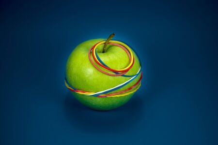 Green apple tied in colorful rubber bands over a blue background. Simplicity back to school or diet, aerobic concept with copy space for textの写真素材