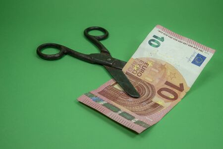 Old vintage scissors cut ten EUR banknote over green background. European Central Bank interest rate cuts conceptの写真素材