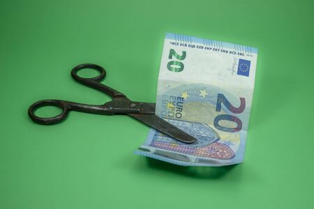 Old vintage scissors cut twenty EUR banknote over green background. European Central Bank interest rate cuts conceptの写真素材