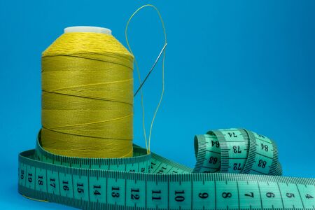 Needlework and tailoring concept - spools of thread and tape measure on blue backgroundの写真素材