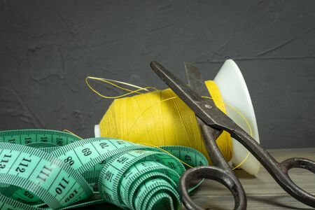 Old metal scissors with tape measure and spools of thread on rustic wooden background, needlework and tailoring conceptの写真素材