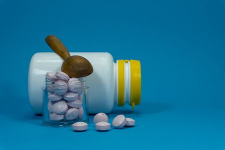 Medicine pills spilling out of a white bottle on a blue backgroundの写真素材