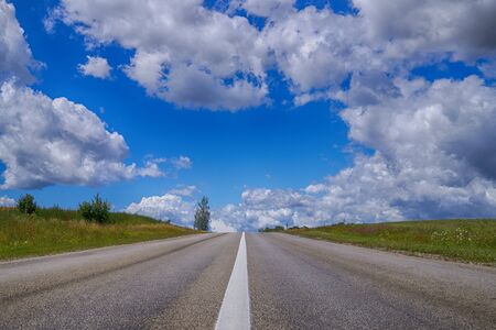 Low angle view of a tarred road receding into the distance in open countryside under a cloudy blue sky with focus to the center white lineの写真素材