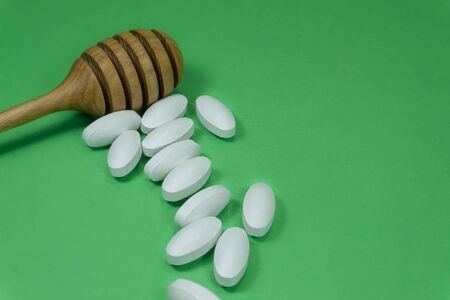 Wooden honey wand with scattered pharmaceutical pills on a colorful green background with copy space in a healthcare conceptの写真素材