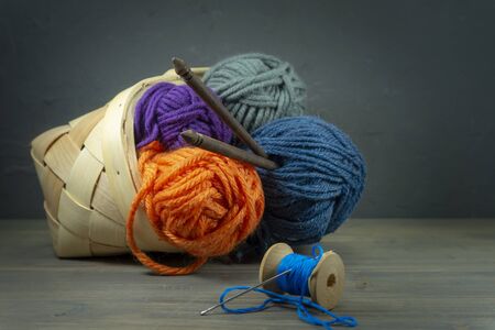 Handicraft and needlework concept - close up of wicker basket with colorful balls of yarn and knitting needles on wooden background with free copy spaceの写真素材
