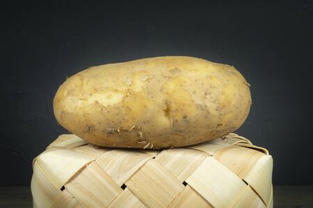 Fresh potato on a tipped wicker basket. Black wall in background, low angle viewの写真素材