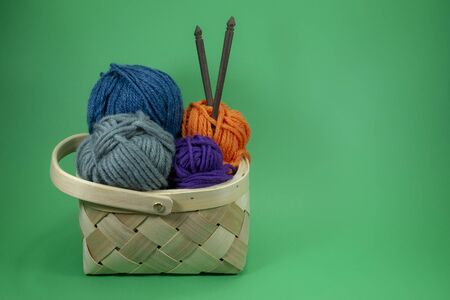 Handicraft and needlework concept - close up of wicker basket with colorful balls of yarn and knitting needles on green background with free copy spaceの写真素材