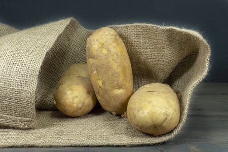 Raw, unwashed, unpeeled potatoes, spilling out of hessian sack on a rustic old wooden backgroundの写真素材