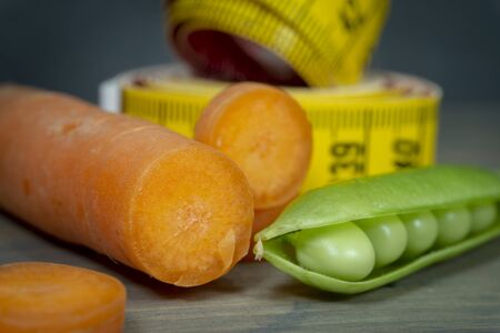 Weight loss and healthy diet concept with carrot, pea pot and measuring tape on wooden backgroundの写真素材