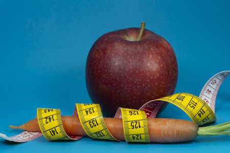 Weight loss and healthy diet concept with measuring tape, carrot and red apple on blue backgroundの写真素材