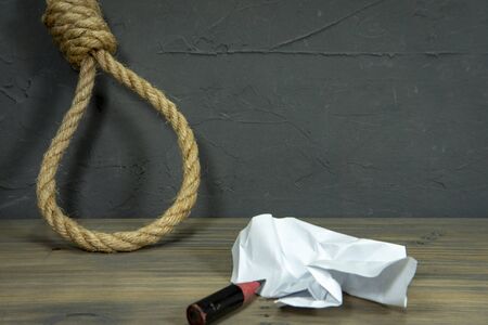 Rope noose around crumpled paper and short stub of a pencil on a rustic wooden table in a conceptual...